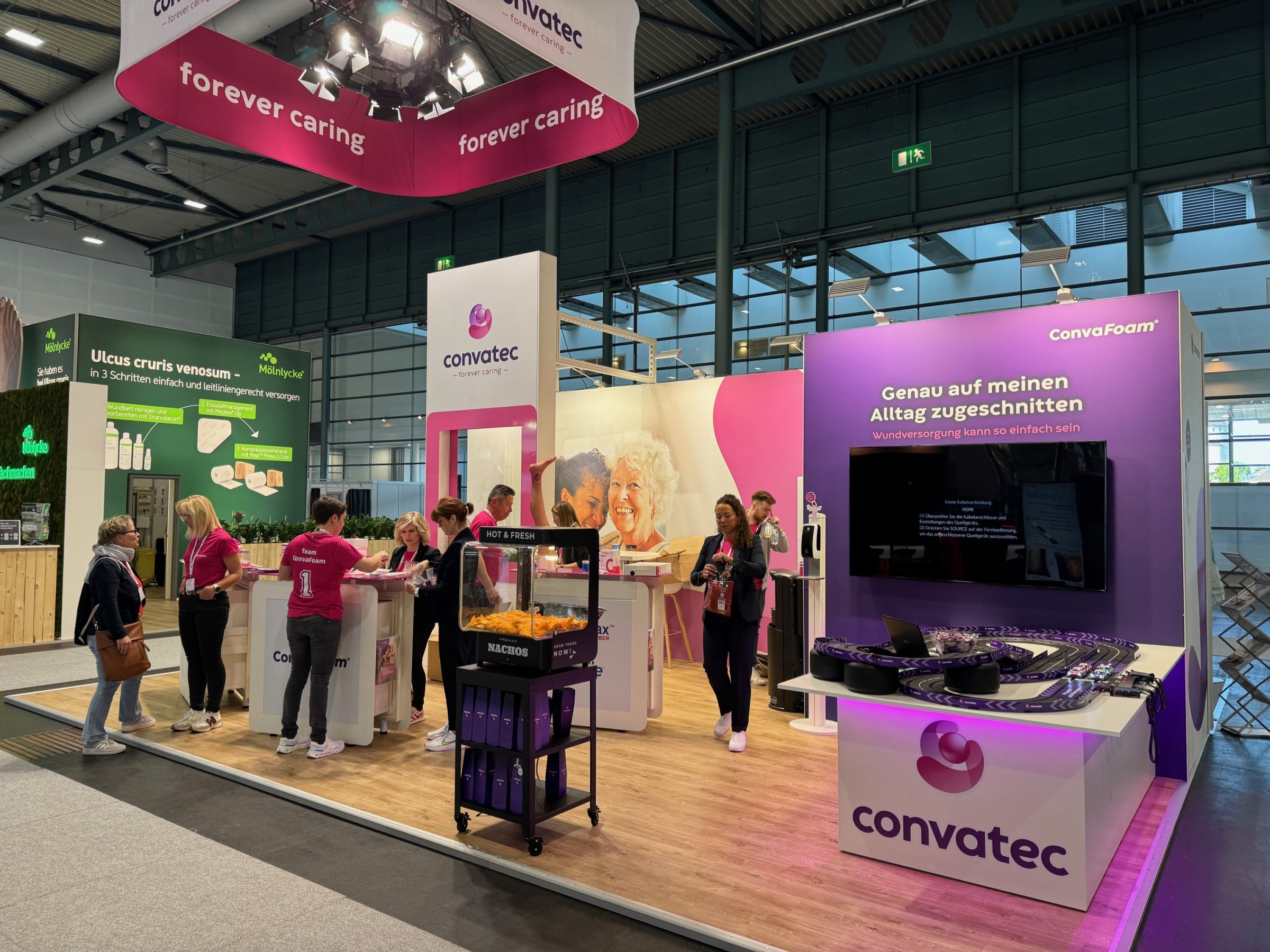Messestand von Convatec mit pinken und violetten Akzenten, Carrera-Bahn und Live-Demonstrationen.