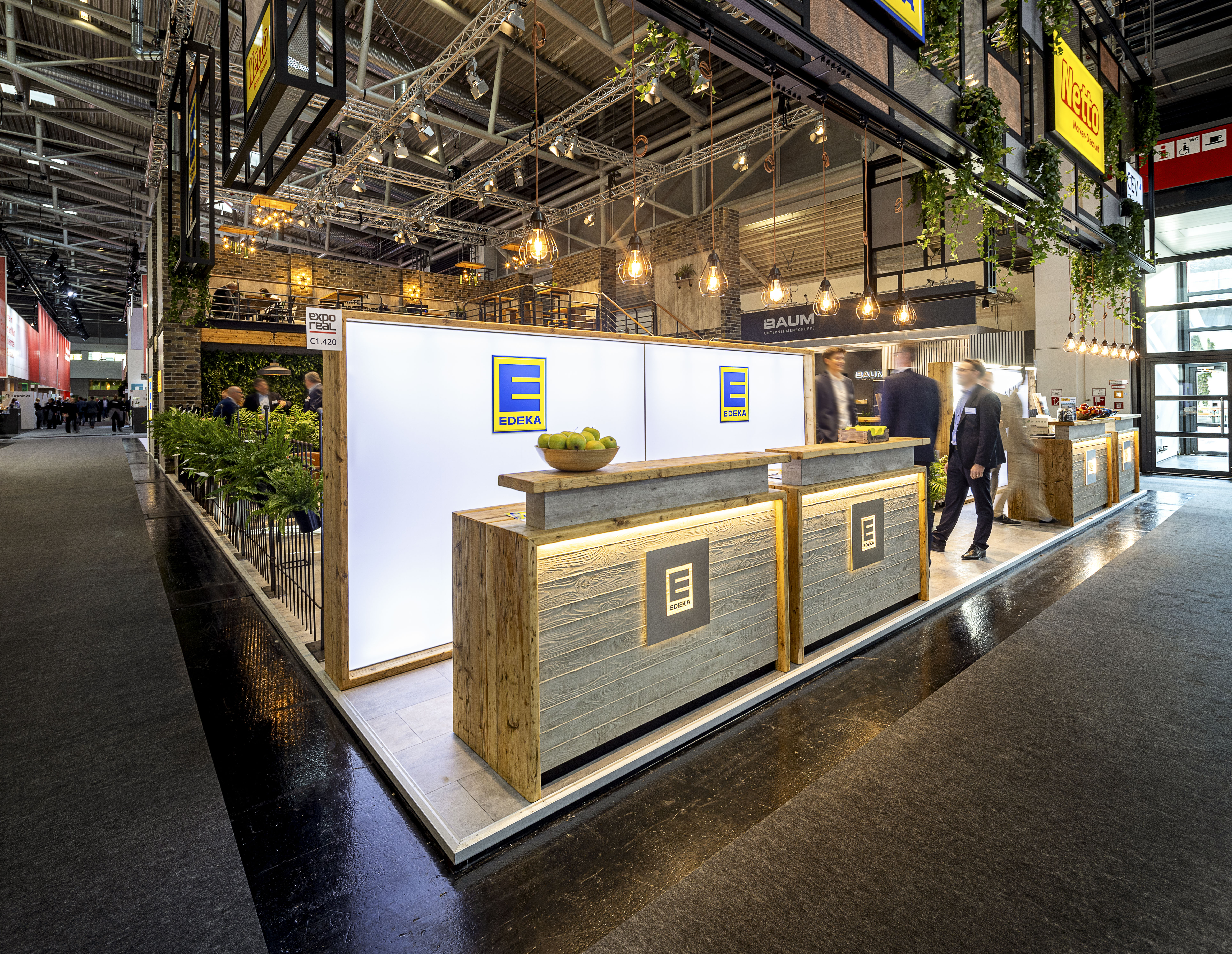 Großer Messeauftritt von EDEKA mit beleuchteten LED-Wänden, Holztheke und Lounge-Bereich auf einer Messe.