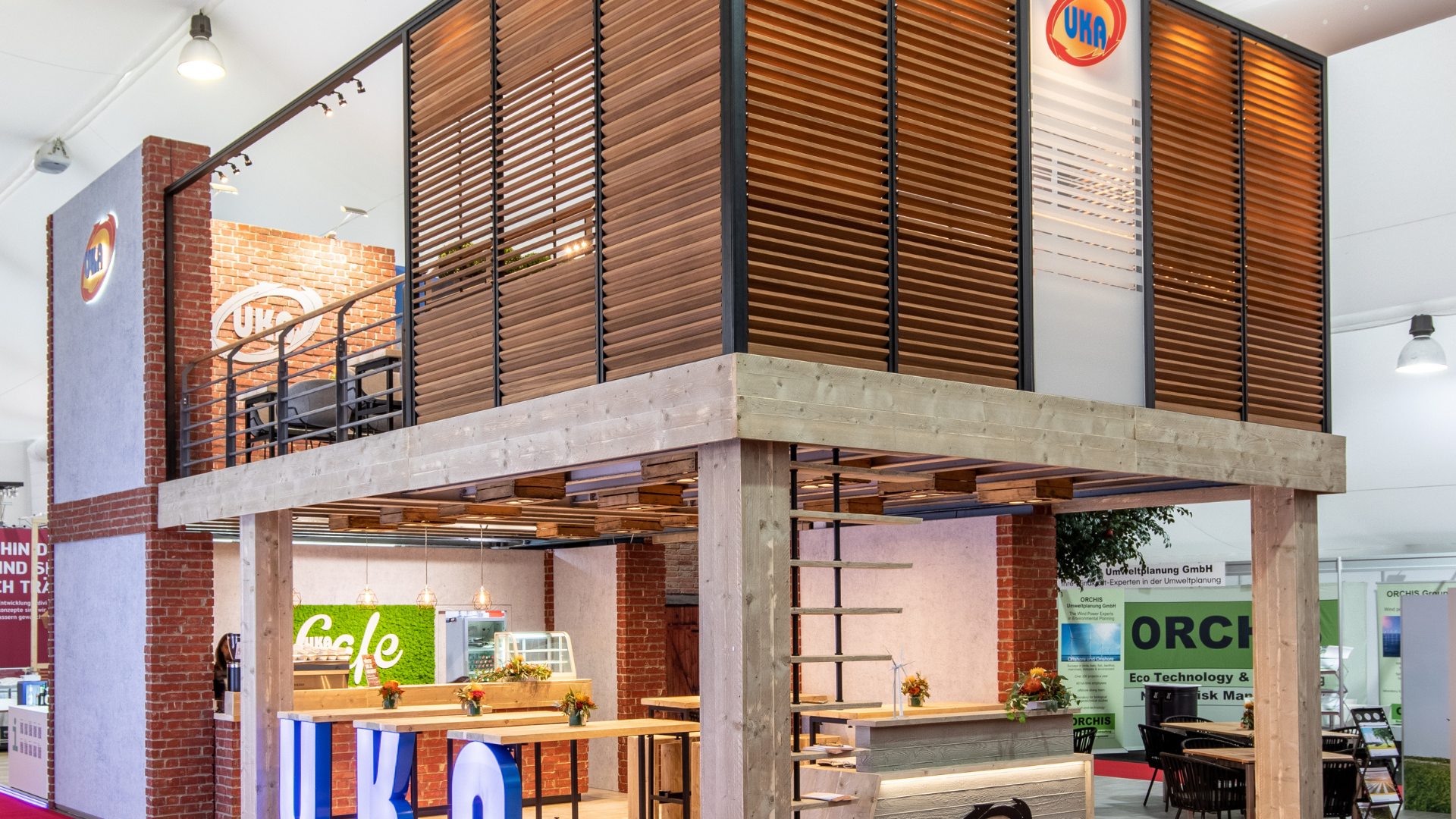 Zweistöckiger Messestand mit Holzlamellen, offener Lounge im Obergeschoss und Sitzbereich im Erdgeschoss auf einer Messe